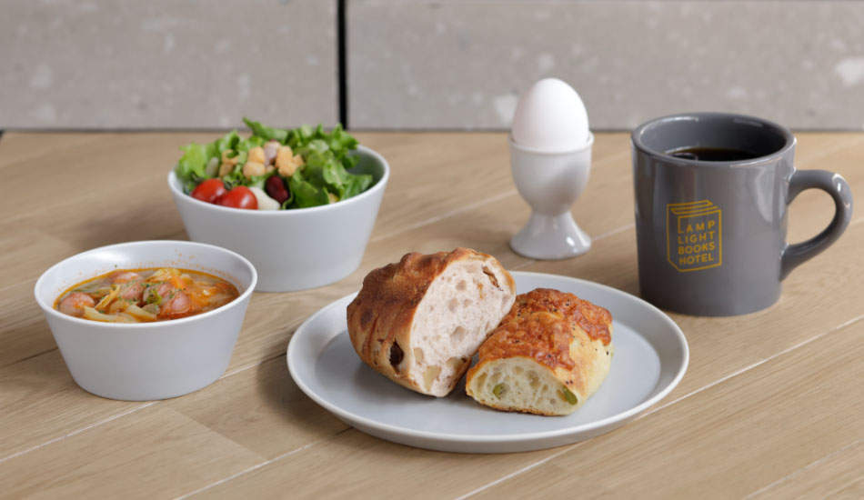 ランプライトブックスホテル札幌の宿泊者限定朝食イメージ写真（パン、スープ、サラダ、半熟卵、ドリンクのセット）